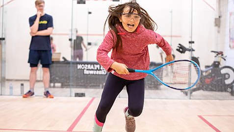 A young girl chasing a ball on a squash court